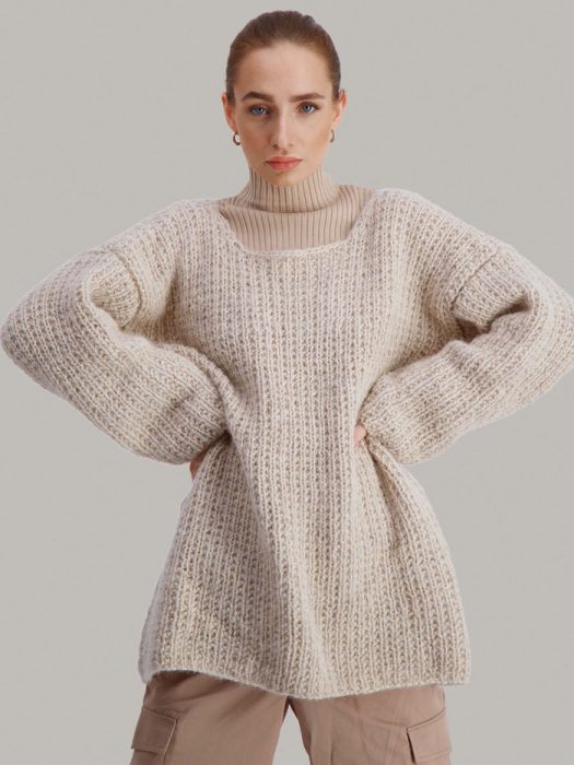 Strikkepakken Dorthegenser fra Skappel Classic. Bilder viser modellen i halvfigur fotografert rett forfra. Modellen holder hendene i siden. Fargen på genseren er sandmelert.