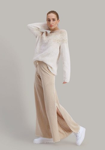 Strikkepakken Flora genser fra Skappel Classic. Bildet viser modellen i helfigur. Modellen står litt sidelengs og ser rett inn i kamera. Høyre hånd ligger på nakken og venstre henger ned langs siden. Fargen på genseren er naturhvit og sandmelert.