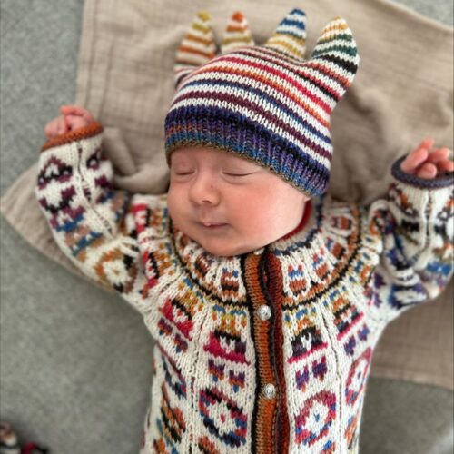 Hentesettet "Velkommen til verden" strikkes i Merino 200 og Merino 200 Color fra Langyarns. Her ser man bildet av den strikkede buksen og sokken på en påkledd baby.