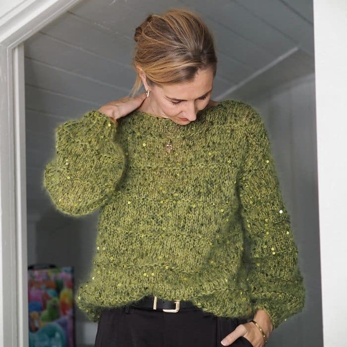 Produktbilde: Modell i front med arm som hviler på skulder. Strikkepakke Holiday sweater designet av Tove Lindtein, strikket i Bella by Permin og Cosmo fra Lana Grossa.